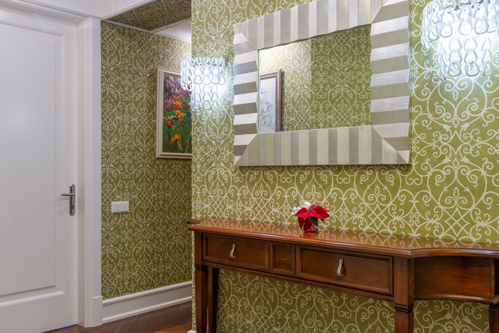 Entryway framed by green damask wallpaper and a warm-wood console