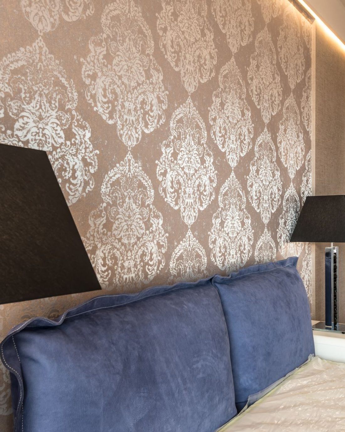 A bedroom feature wall in taupe damask wallpaper behind a velvet headboard