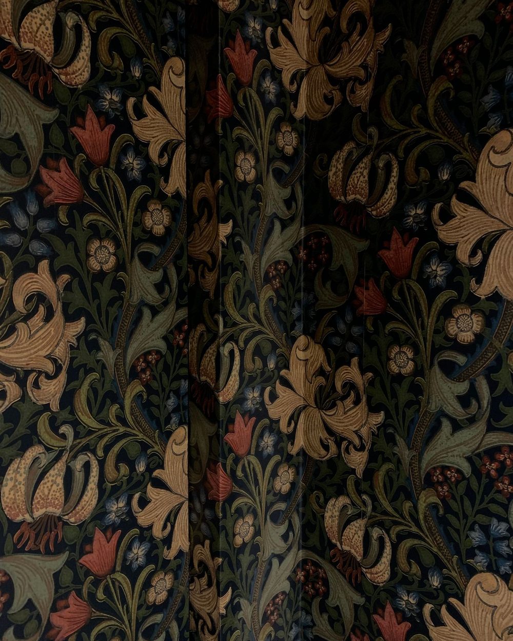 A richly patterned wallpaper in deep green and gold botanical motifs
